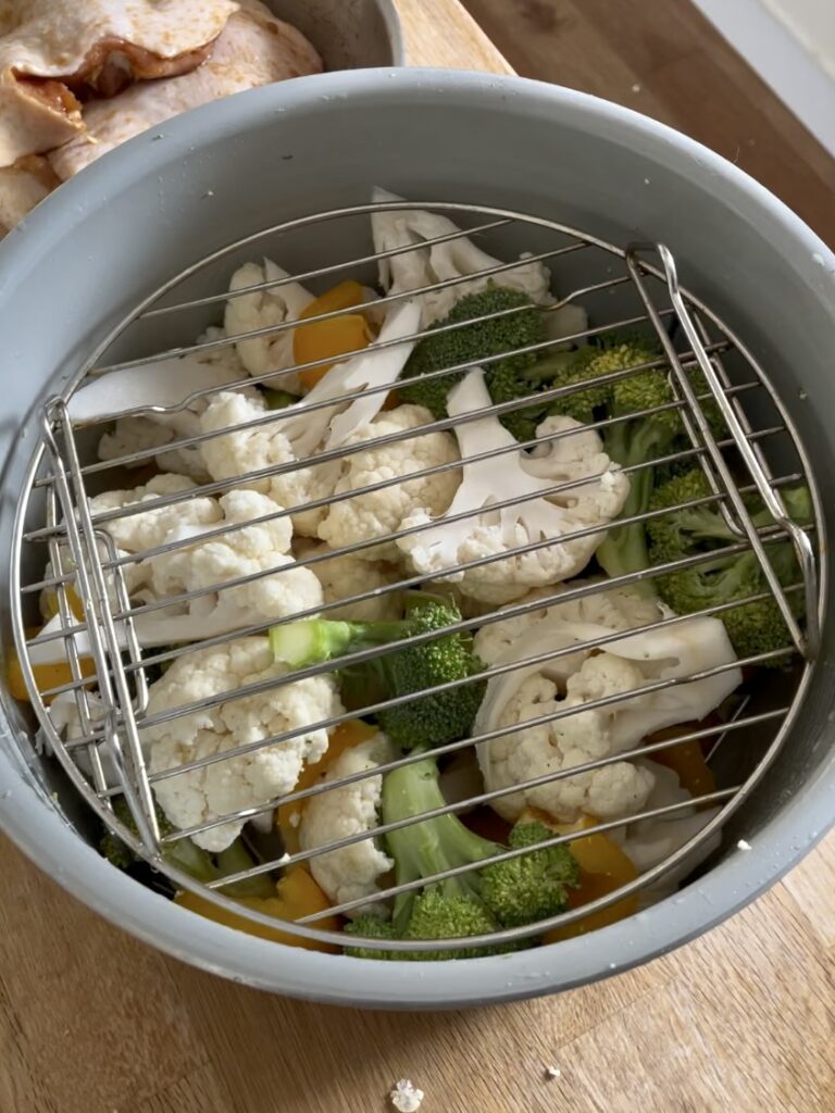 Mix vegetables (cauliflower, broccoli, and bell pepper) in the air fryer base with a metal rack on top.